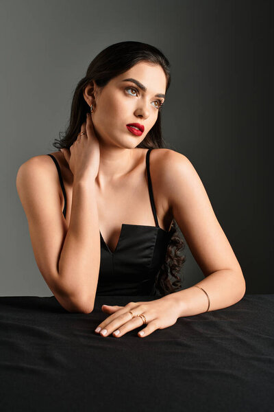 Поразительная молодая женщина с каштановыми волосами и красными губами элегантно позирует.