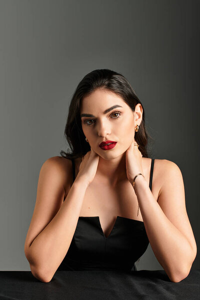 Красивая молодая женщина с каштановыми волосами и смелыми красными губами демонстрирует уверенность в минималистской обстановке.