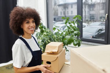 Bir kadın büyük pencereli, parlak ve modern yaşam alanına memnuniyetle paketleri yerleştirir..