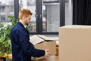 Adam, parlak bir uzayda karton kutulara eşyalarını koymaya odaklanırken görülüyor.