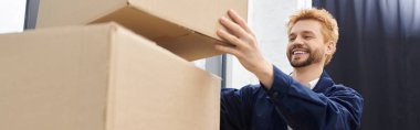 Neşeli bir adam modern bir ortamda karton kutuları toplar ve açar..