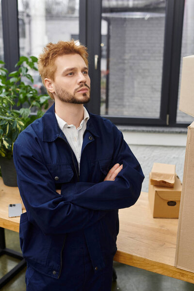 A young man stands thoughtfully in a modern space filled with boxes during packing.