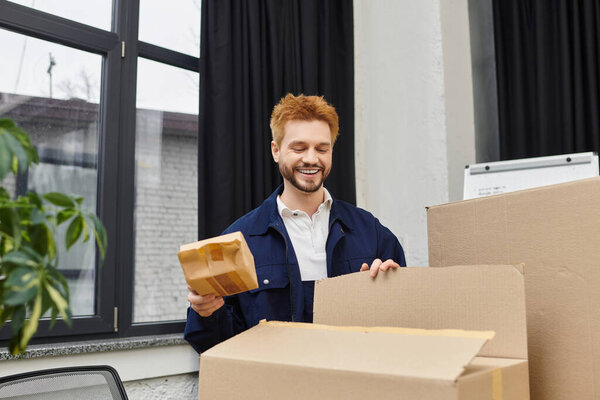 A cheerful man unpacks moving boxes in a stylish office setting, organizing belongings.