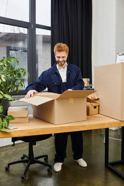 A man joyfully unpacks cardboard boxes in a contemporary office filled with plants and sunlight.