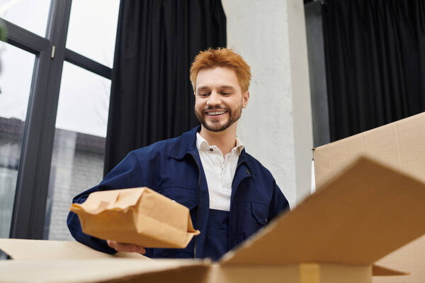 A cheerful man unpacks boxes and sorts items in a modern space.