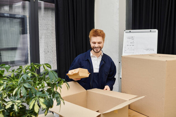 A cheerful man carefully unpacks boxes in a stylish indoor environment filled with plants.