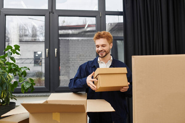 A man smiles while unpacking boxes in a contemporary room filled with light and greenery.