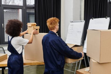 İki kişi, takım çalışması sergileyerek, modern bir çalışma alanında kutuları paketleyip açıyor..