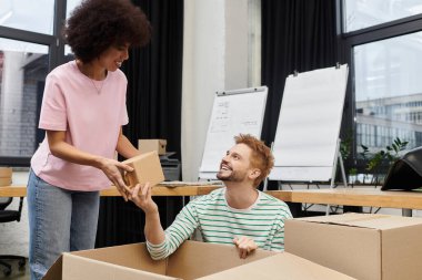 Çift, çağdaş bir ofis ortamında kutuları paketlerken neşeli bir anı paylaşıyor.