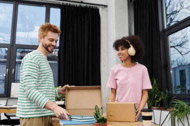 İki arkadaş mutlu bir şekilde, parlak ve çağdaş bir çalışma alanında kutuları açıp paketlemekle meşguller..