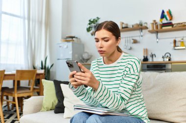 Kanepede oturan genç bir kadın rahat ve modern bir ortamda akıllı telefonuna odaklanıyor..