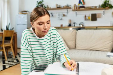 Genç bir kadın modern bir dairede masada oturuyor, notlar yazıyor ve öğleden sonra eğleniyor..