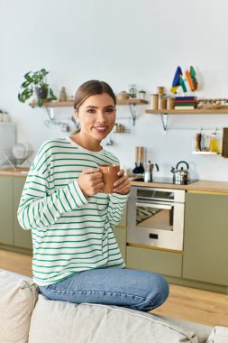 Genç ve güzel bir kadın, şık mutfağında dinlenirken kanepede oturup kahvesini yudumluyor..