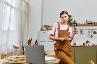 Genç bir kadının elinde defterle ders çalıştığı bitkilerle dolu parlak, modern bir mutfak..