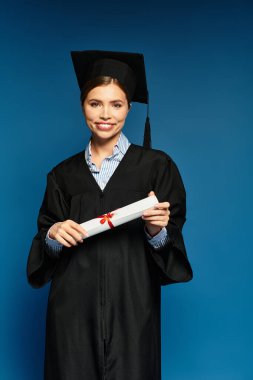 Elbise giymiş genç bir kadın gururla diplomasını kırmızı kurdeleyle tutuyor..