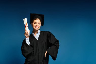 Mezuniyet elbisesi içinde gururlu bir kadın diplomasını tutuyor, nefes kesici bir şekilde gülümsüyor..