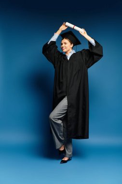 Mutlu genç bir kadın mezuniyet elbisesi giyerek diplomasını yükseltiyor ve başarısını gösteriyor..