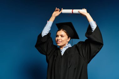 Mezuniyet kıyafetli neşeli genç bir kadın bir kutlama anında diplomasını yüksek tutuyor..