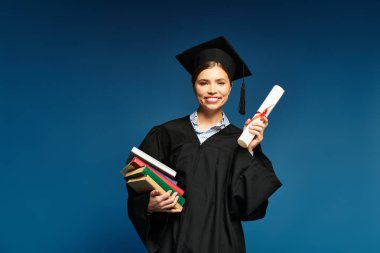 Mezuniyet kıyafetli neşeli genç kadın diploma ve kitap taşıyor, mutluluk ve başarı saçıyor..