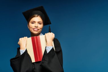 Neşeli mezun, kep ve cübbe giyerek kitabı sıkıca tutuyor..