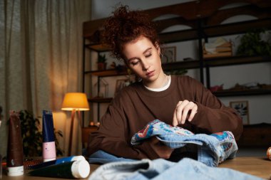 Genç bir kadın şık çalışma alanındaki kot pantolona renkli desenler çiziyor..