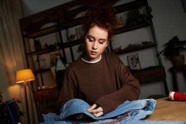 Genç zanaatkar kadın rahat bir atmosferde kot pantolonu kişiselleştirilmiş tasarımlara dönüştürüyor..