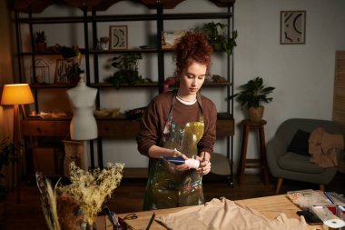 Genç ve güzel bir kadın sanatsal aletler ve dekorasyonla çevrelenmişken yaratıcı bir zanaatla meşgul oluyor..