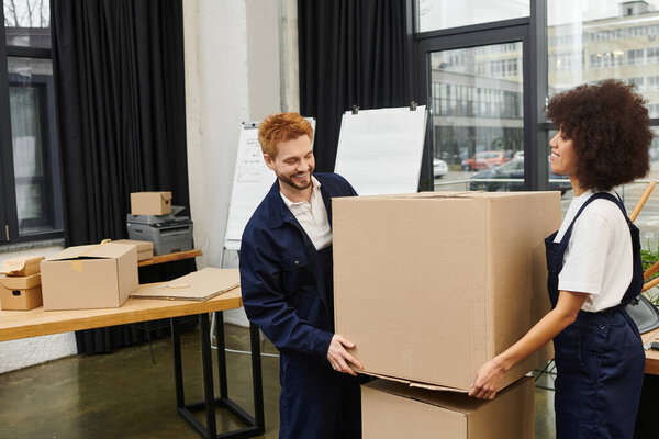 Two movers enthusiastically handle large cardboard boxes while organizing a contemporary workspace.