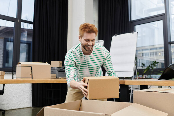 A man joyfully packs boxes while preparing to move into a bright, modern office environment.