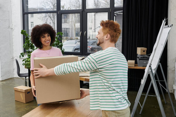Friends collaborate to pack and unpack boxes in a contemporary office environment, sharing smiles.