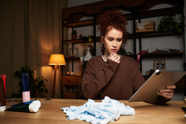 Молодая женщина исследует новые конструкции на планшете в окружении ремесел в теплой комнате.