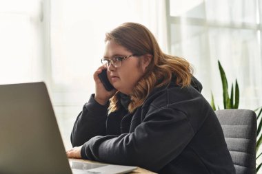 Rahat bir evde, Down sendromlu genç bir kadın dizüstü bilgisayarını kullanırken telefonla konuşuyor..