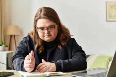 Down sendromlu genç bir kadın evinde bir masada otururken ders çalışıyor..