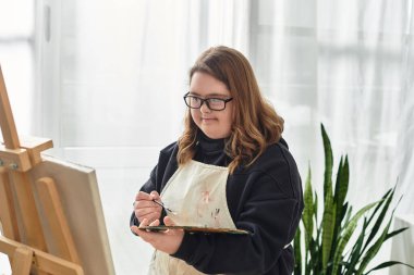 Down sendromlu genç bir kadın evde resim yapmaya odaklanmış yaratıcılığını ifade ediyor..