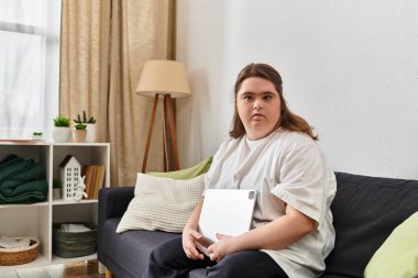 Down sendromlu kendine güvenen genç bir kadın kanepede oturup tabletiyle meşgul olur..