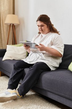 Rahat bir evde, Down sendromlu genç bir kadın kanepede rahatlar, kitabında kaybolur..