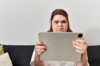 Down sendromlu genç bir kadın evde rahatlıyor, tabletine odaklanıyor..