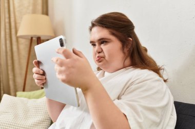 Down sendromlu kendine güvenen genç bir kadın evde tabletini kullanırken bir anlık keyfine bakıyor..