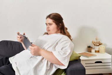 Down sendromlu genç bir kadın rahat bir evde tabletini kullanıyor..