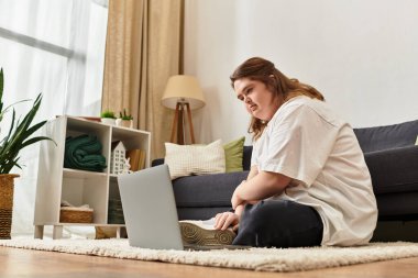 Down sendromlu genç bir kadın evinde dizüstü bilgisayarını kullanarak yerde dinleniyor..