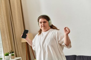 Genç kadın evde rahat, kulaklıkla dans ediyor, telefonunu tutuyor, mutluluk saçıyor..