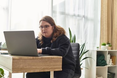 Down sendromlu kendine güvenen genç bir kadın masasında rahat bir evde çalışıyor..