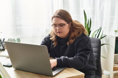 Down sendromlu genç bir kadın evinde rahatça otururken dizüstü bilgisayarına odaklanır..