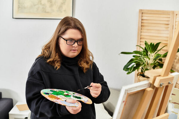 Яркое утро дома, как уверенная молодая женщина с синдромом Дауна создает искусство на холсте.