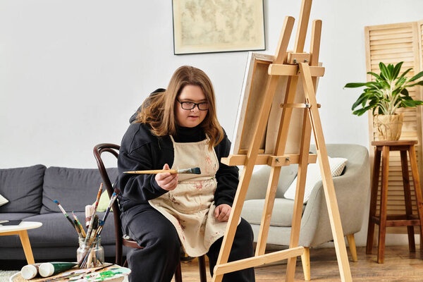 Молодая женщина с синдромом Дауна фокусируется на живописи в хорошо оформленном жилом помещении.