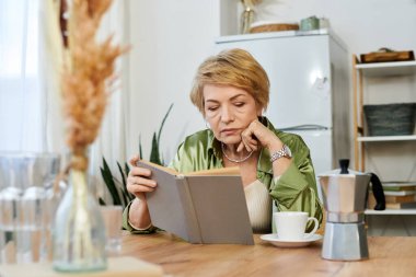 Hoş bir son sınıf öğrencisi, ahşap bir masada rahatlar, kahvesini yudumlar ve bir kitaptan zevk alır..