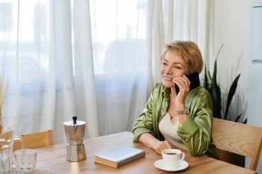 Güzel olgun bir kadın telefonda konuşurken gülümsüyor. Etrafı sıcak mutfak atmosferiyle çevrili..