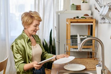 Güzel, kıdemli bir kadın, parlak mutfağında bulaşıkları yıkarken nazikçe gülümser..