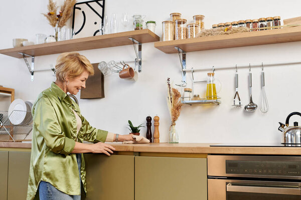 Senior woman with a beautiful smile interacts with her kitchen space, preparing a delightful meal.