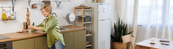 In a bright kitchen, a lovely senior woman arranges flowers on the counter.